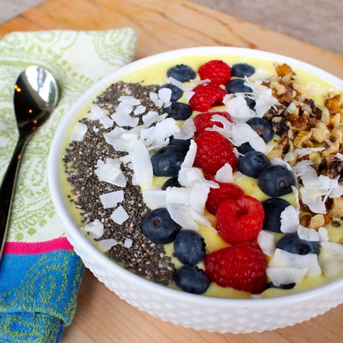 The yellow tropical detox smoothie bowl topped with raspberries, blueberries, coconut flakes, and chia seeds.