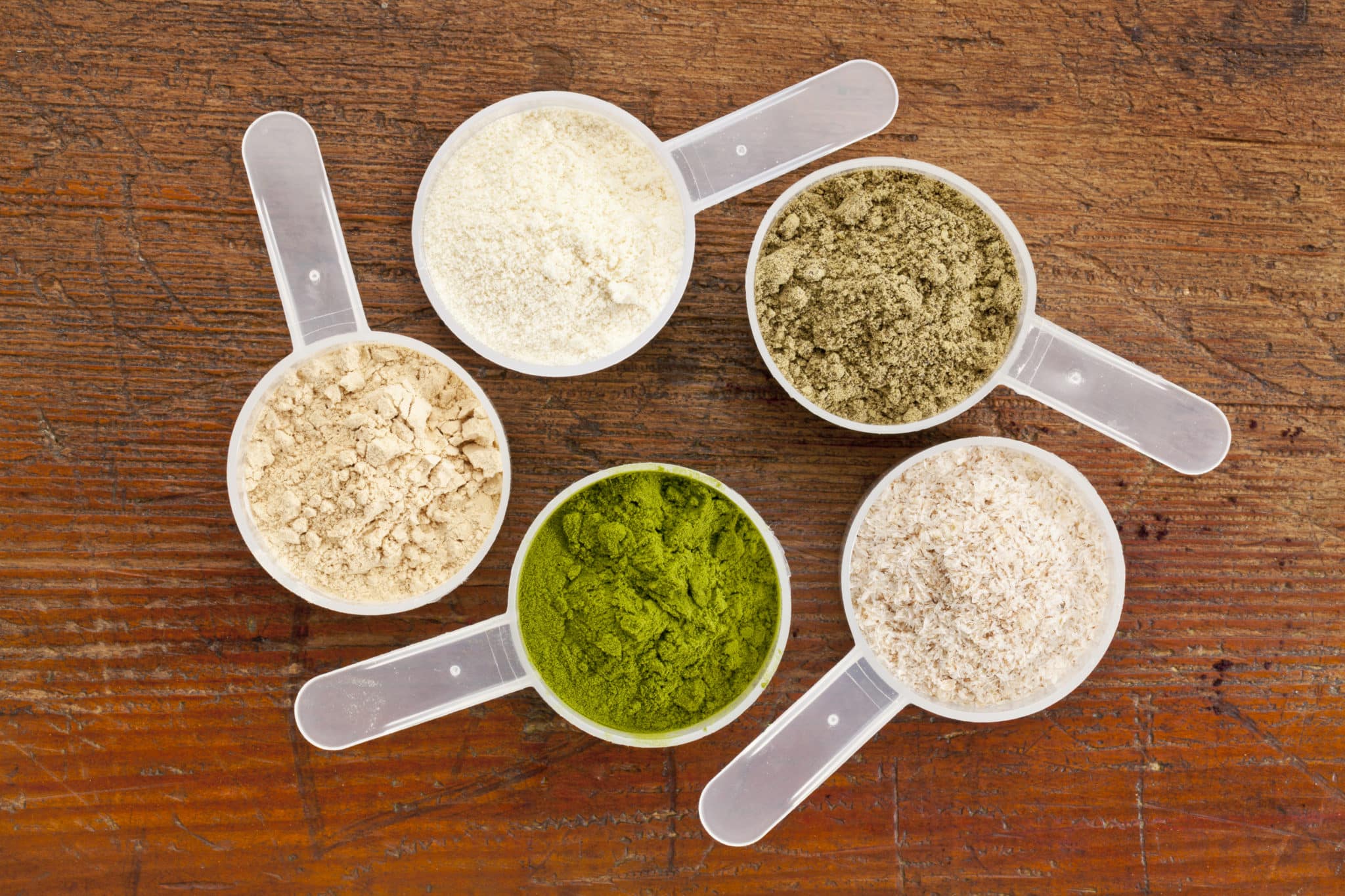 Five scoops of plant based protein powders on wood table