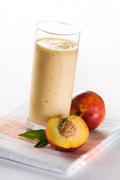 Apple peach crisp smoothie in a tall glass with a peach in the forefront