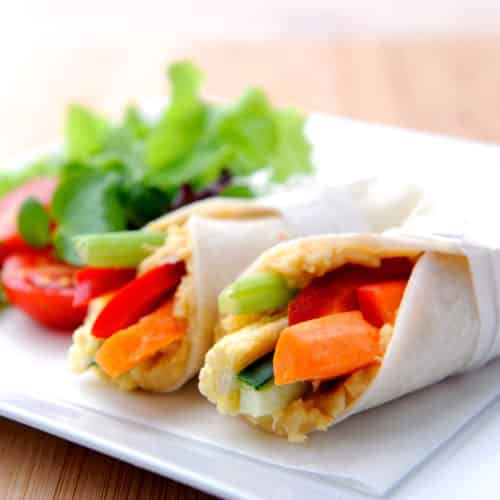 Tortilla wraps with fresh veggies and hummus on white plate