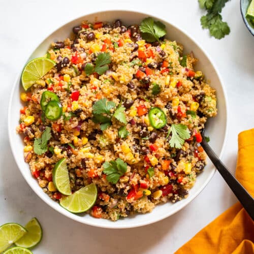 single southwest quinoa salad serving in white bowl with fork on white countertop background
