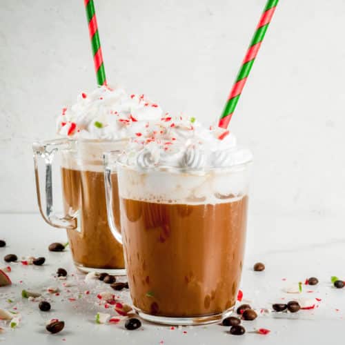 Two glass mugs with peppermint mocha and coconut cream on top with holiday straws