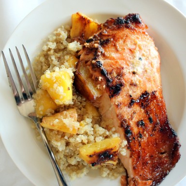 a white plate with brown sugar glazed salmon and caramelized pineapple quinoa