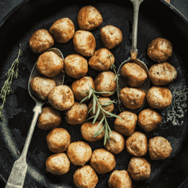 Ground chicken meatballs in a cast iron pan with spoons and a sprig of rosemary