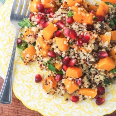 a yellow plate with quinoa salad with chunks of squash, pomegranate, seeds, and Dijon dressing
