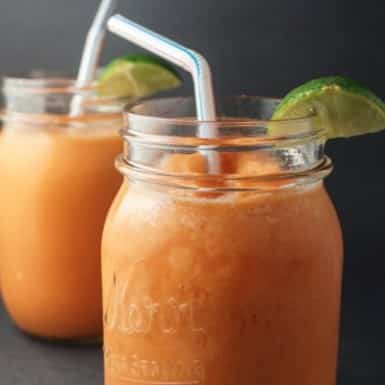 Carrot Orange Mango Smoothie divided into two mason jar glasses with a lime wedge and straw in each.