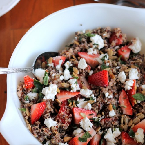 A white bowl filled with a quinoa salad with strawberries and feta