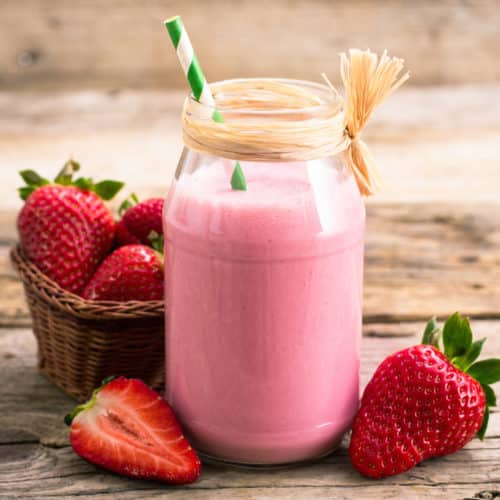 A glass filled with a strawberries and cream dessert smoothie with strawberries around it