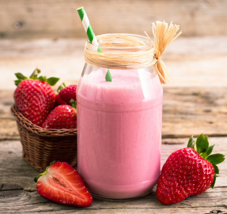 A glass filled with a strawberries and cream dessert smoothie with strawberries around it