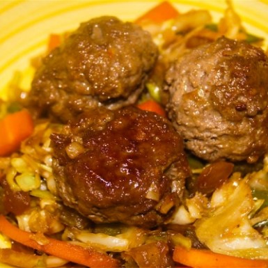 Asian Meatballs on top of a bed of coleslaw on a yellow plate.