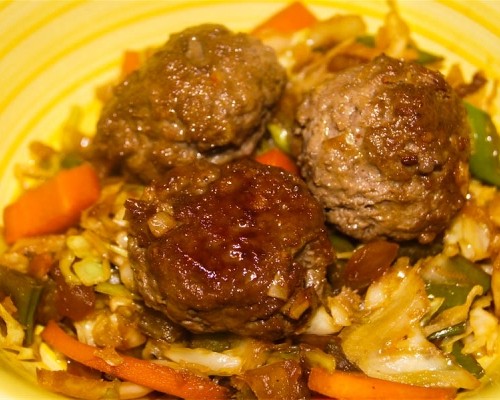 Asian Meatballs on top of a bed of coleslaw on a yellow plate.