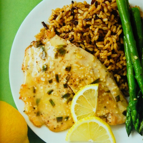 A white plate with whitefish filet covered in a tarragon sauce one abed of brown rice and side of steamed asparagus