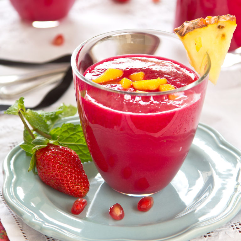 Pomegranate, ginger and pineapple smoothie in a glass sitting on a light blue plate