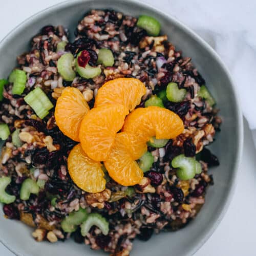 An off-white bowl of wild rice salad with mandarin oranges, celery and cranberries.
