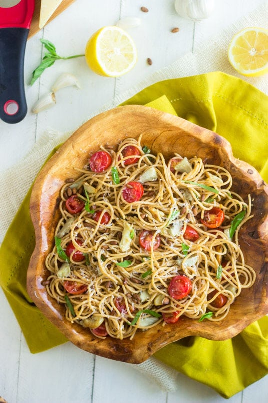 a large wooden bowl filled with pasta salad with tomato, artichokes, and vinaigrette
