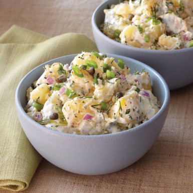 two blue bowls filled with creamy potato salad garnished with green onion