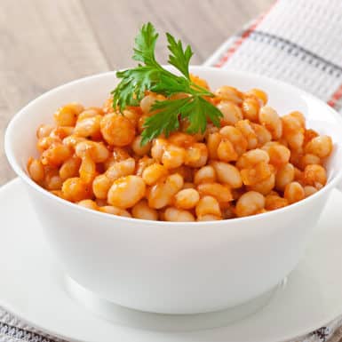 A white bowl filled with baked beans in a brown sauce