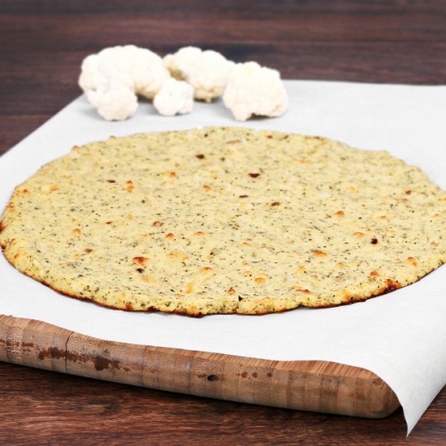 Plain cauliflower pizza crust on a piece of parchment paper on a cutting board. Selective focus on front edge of crust.