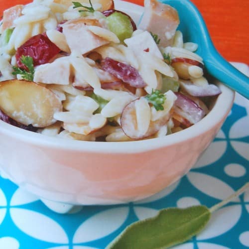 A white bowl filled with creamy orzo salad with cherries and almonds