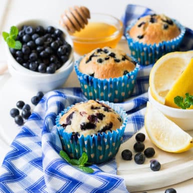 Lemon blueberry muffins on white plate surrounded by fresh blueberries, honey and lemon slices