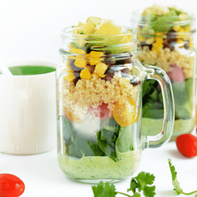 a mason jar layered with a green salad, corn and avocado