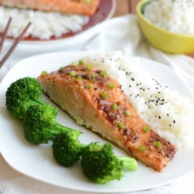 a white plate with a seasoned salmon filet topped with a glaze and side of broccoli and rice