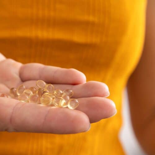 woman holding pile of vitamin d supplements in her hand with orange shirt