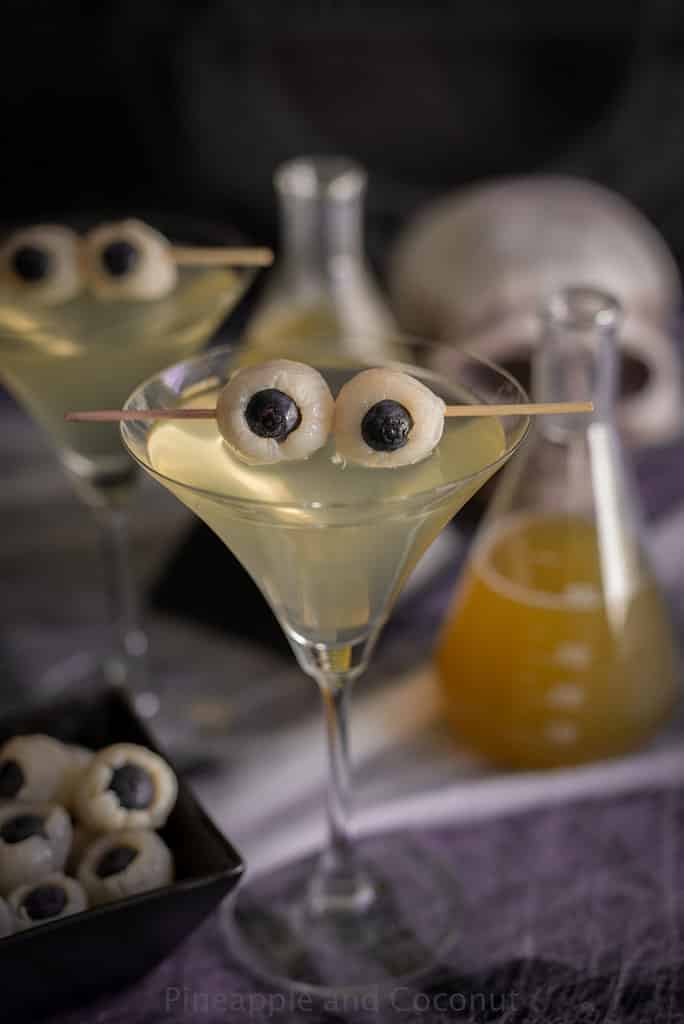 A Creepy Eyeball Martini on a table with a flask and viles to make it look spooky for Halloween.