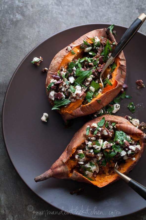 Baked Sweet Potatoes Stuffed with Feta, Olives, and Sundried Tomatoes on a black plate.