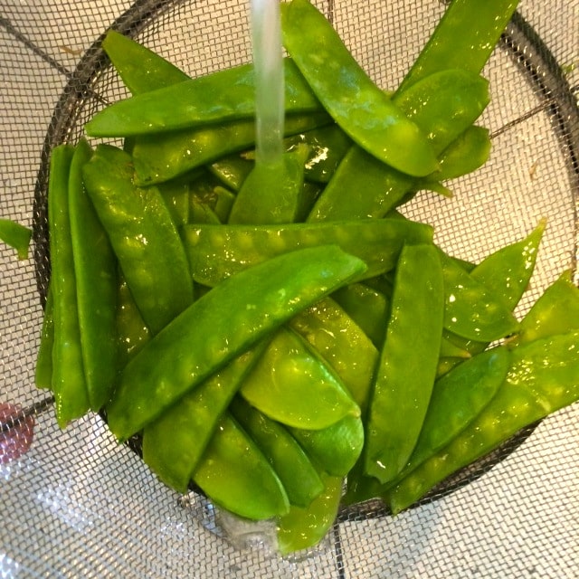 a strainer with snow peas being rinsed off