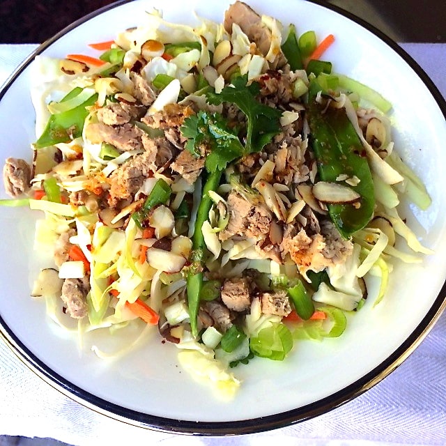 a Asian salad with cabbage, snow peas, and carrots covered with pulled pork and ginger sesame dressing