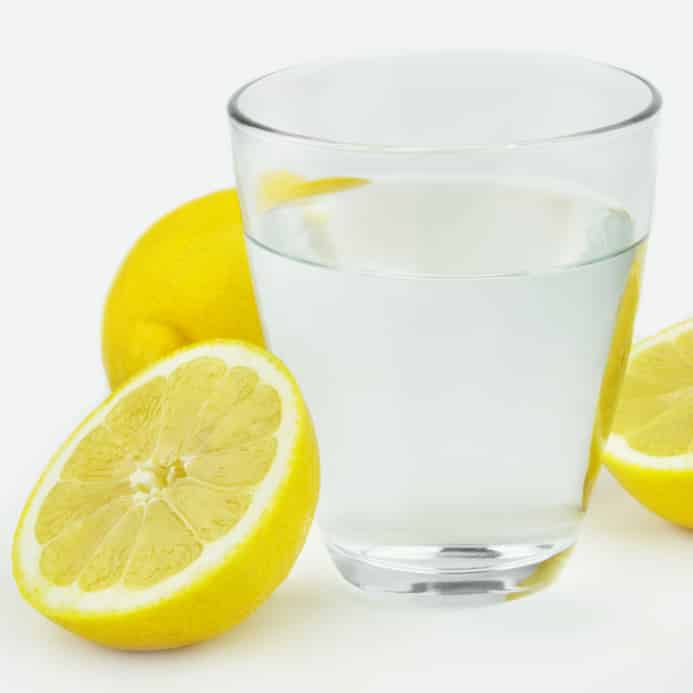 A glass of lemon water with lemons around it