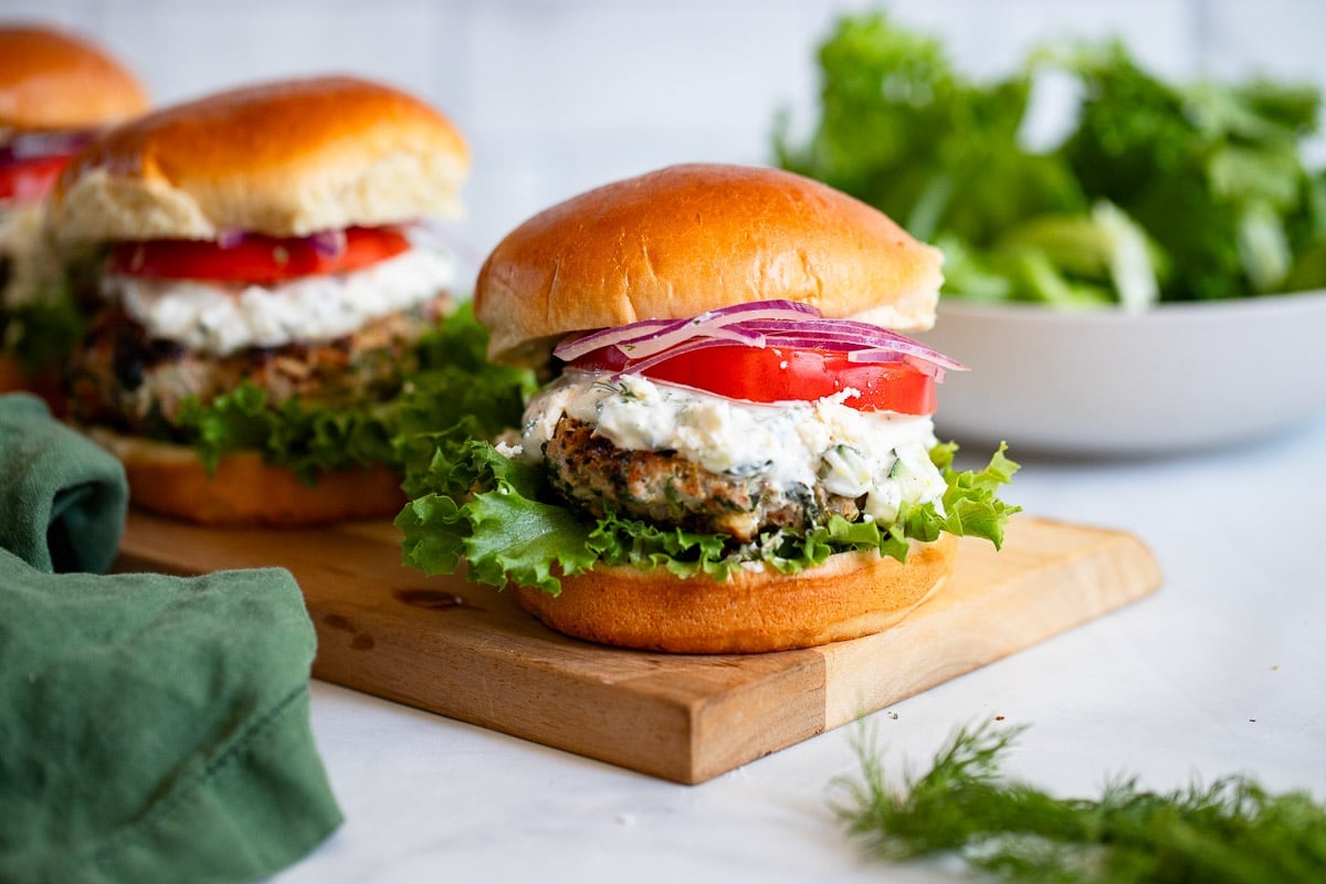greek turkey burgers with toppings on wooden serving board on white counter