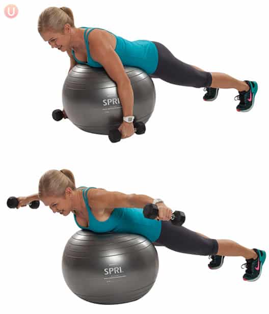 Chris Freytag demonstrating a rear delt raise on a stability ball wearing black yoga pants and a blue top.