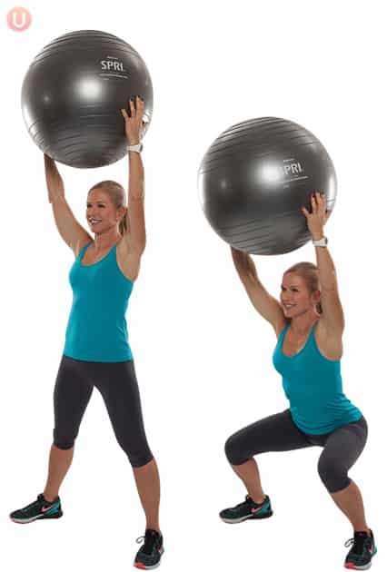 Chris Freytag demonstrating a squat holding a stability ball wearing black yoga pants and a blue top