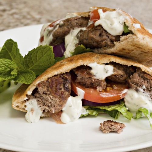 a white plate with pita bread pockets filled with Greek turkey burgers drizzled with yogurt cucumber dressing