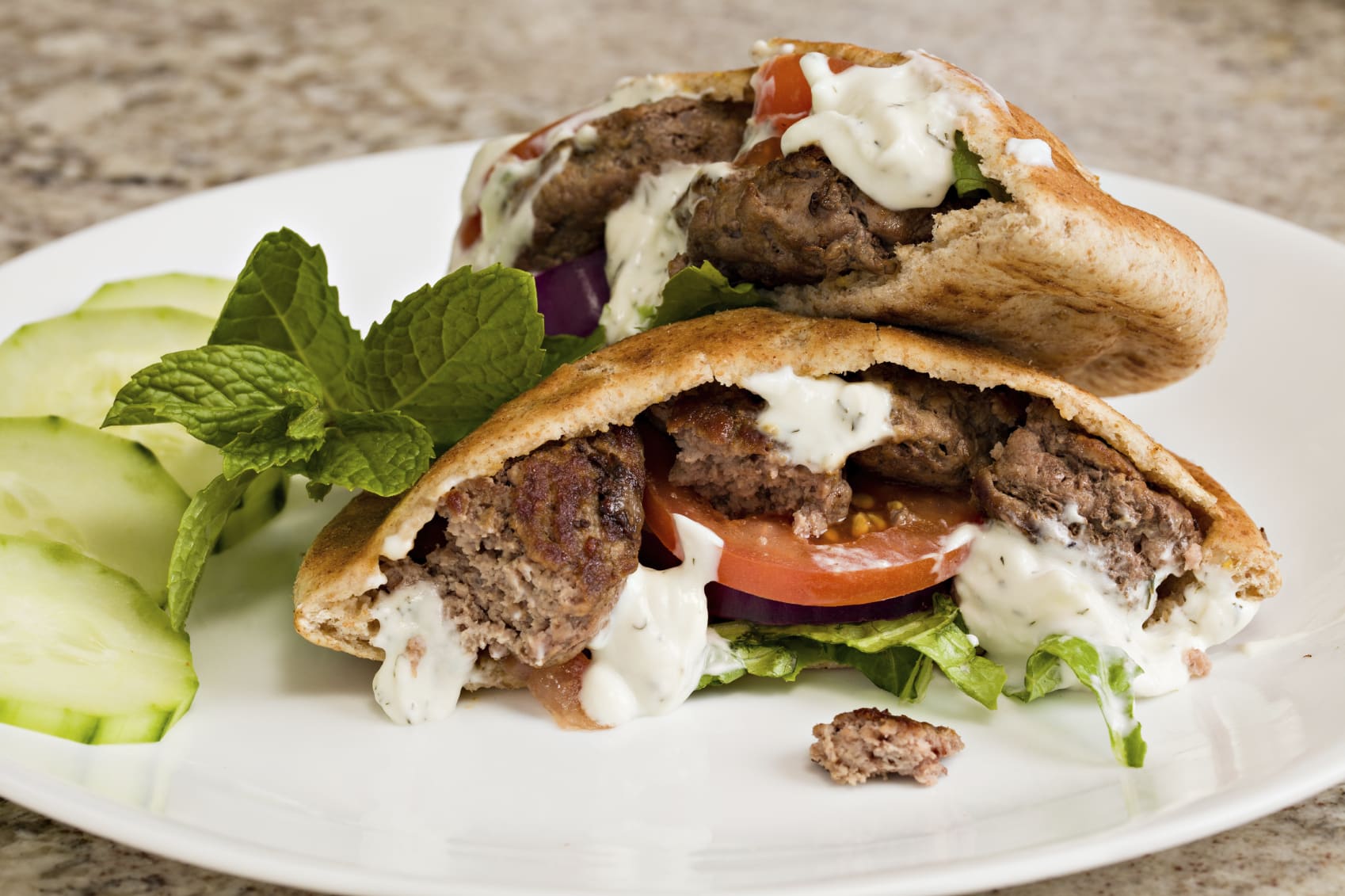 a white plate with pita bread pockets filled with Greek turkey burgers drizzled with yogurt cucumber dressing