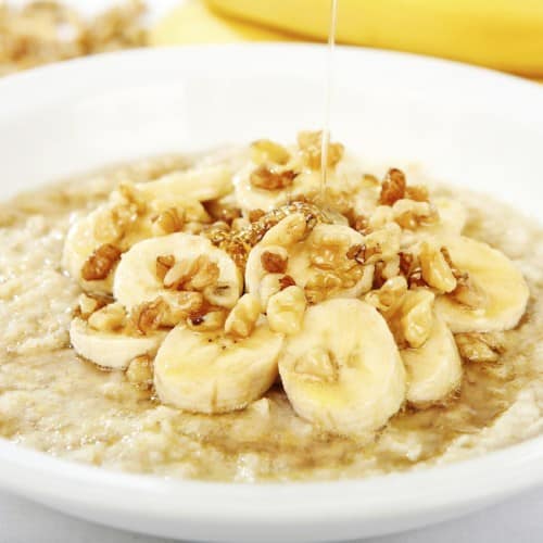 A bowl of banana nut oatmeal and walnuts and honey being drizzled over it