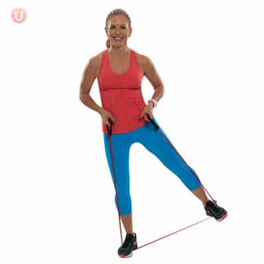 Chris Freytag demonstrating a resistance band tick tock exercise wearing a red top and blue exercise pants.