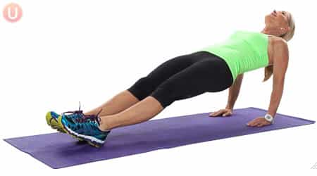 Chris Freytag demonstrating a reverse plank in a green tank top on a purple yoga mat.