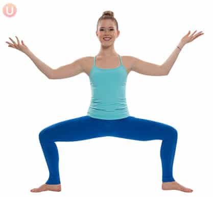 Chloe Freytag demonstrating Sun God Pose in a blue tank top and yoga pants