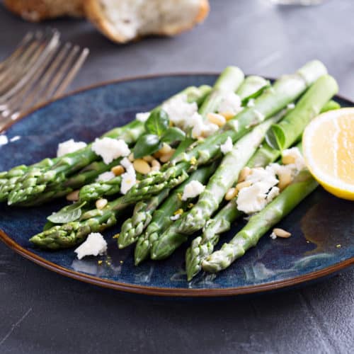 A blue plate with asparagus and crumbled feta. Garnished with lemon.