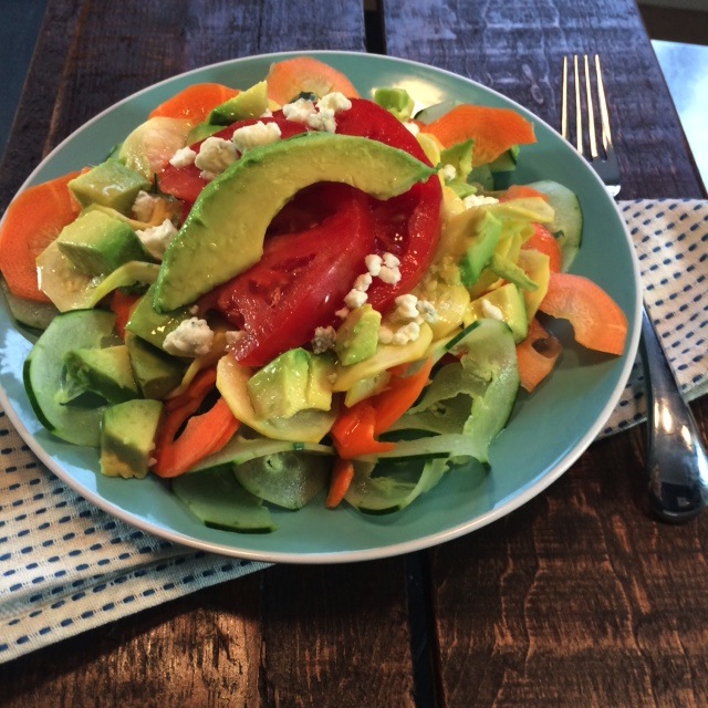 A plate filled with spiralized vegetable noodles topped with avocado and blue cheese crumbles.
