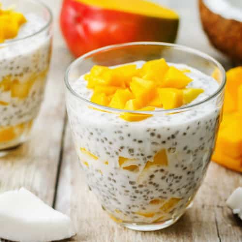 A cup of coconut chia seed pudding with mango on whitewashed wood