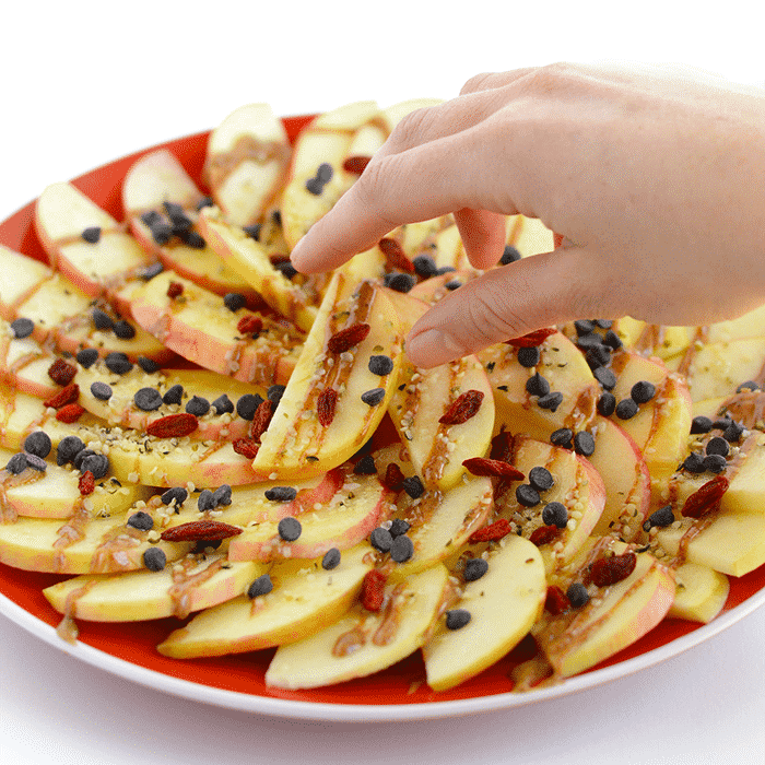 Healthy Apple Nachos Appetizer Recipe on a red plate with a hand reaching in.