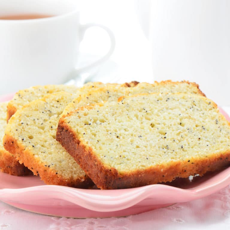 Slices of lemon poppyseed cake on a pink plate with coffee in the background