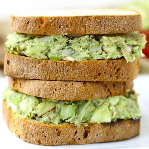 Two healthy tuna sandwiches stacked on each other made with avocado. and served on whole grain bread.