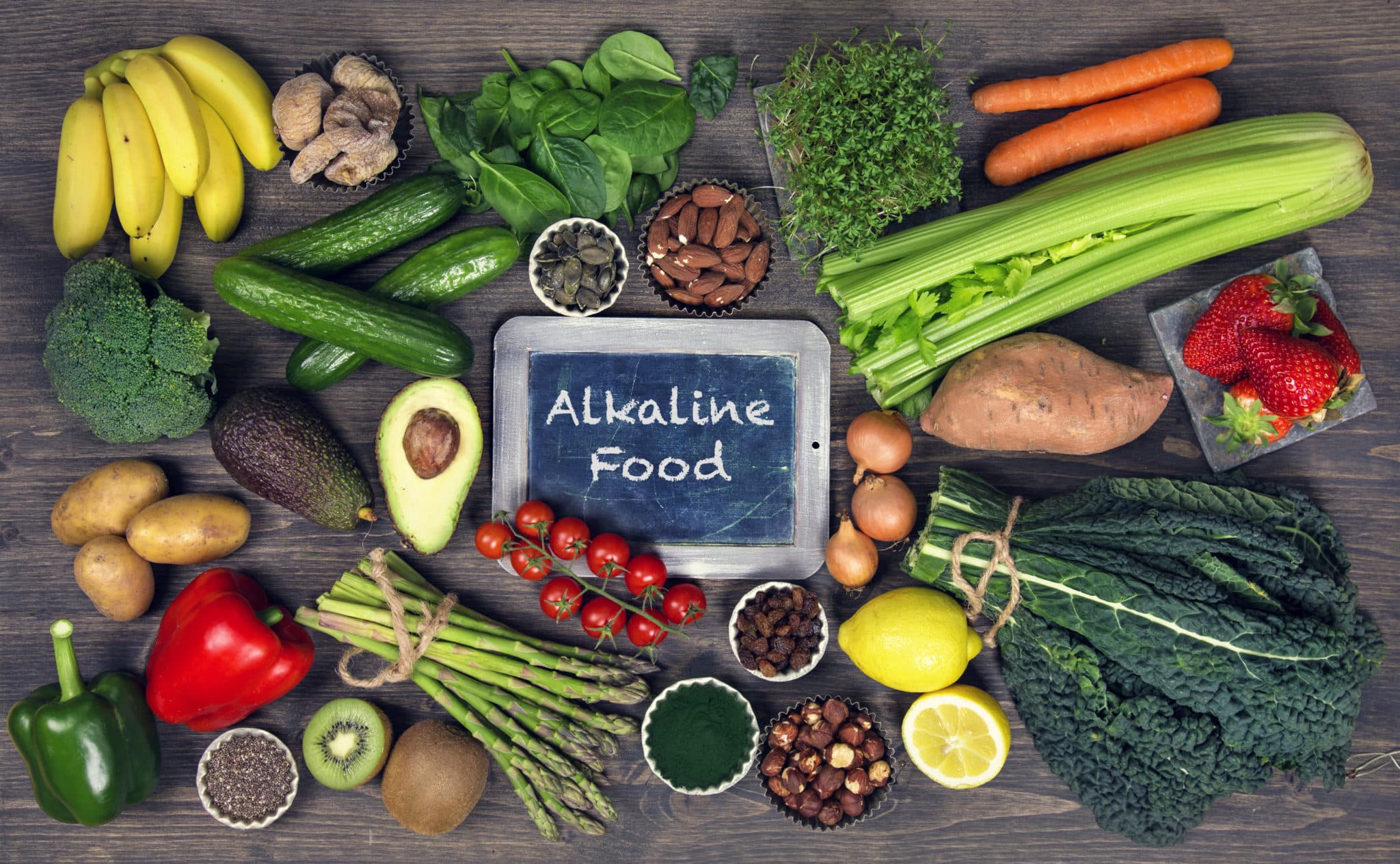 Various fruits and vegetables on dark surface with chalkboard in the middle reading "Alkaline Food"