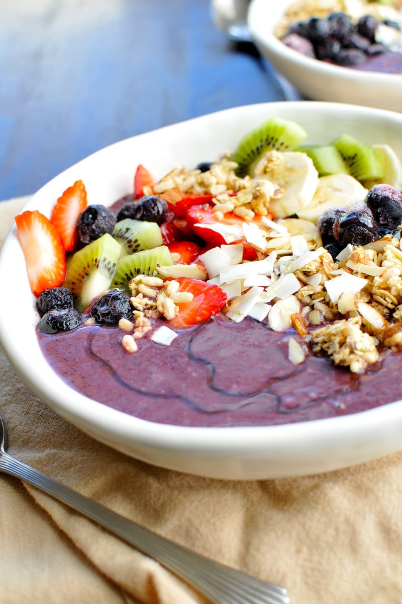 A purple acai smoothie bowl topped with strawberries, kiwi, bananas, coconut chips, blueberries, and granola.