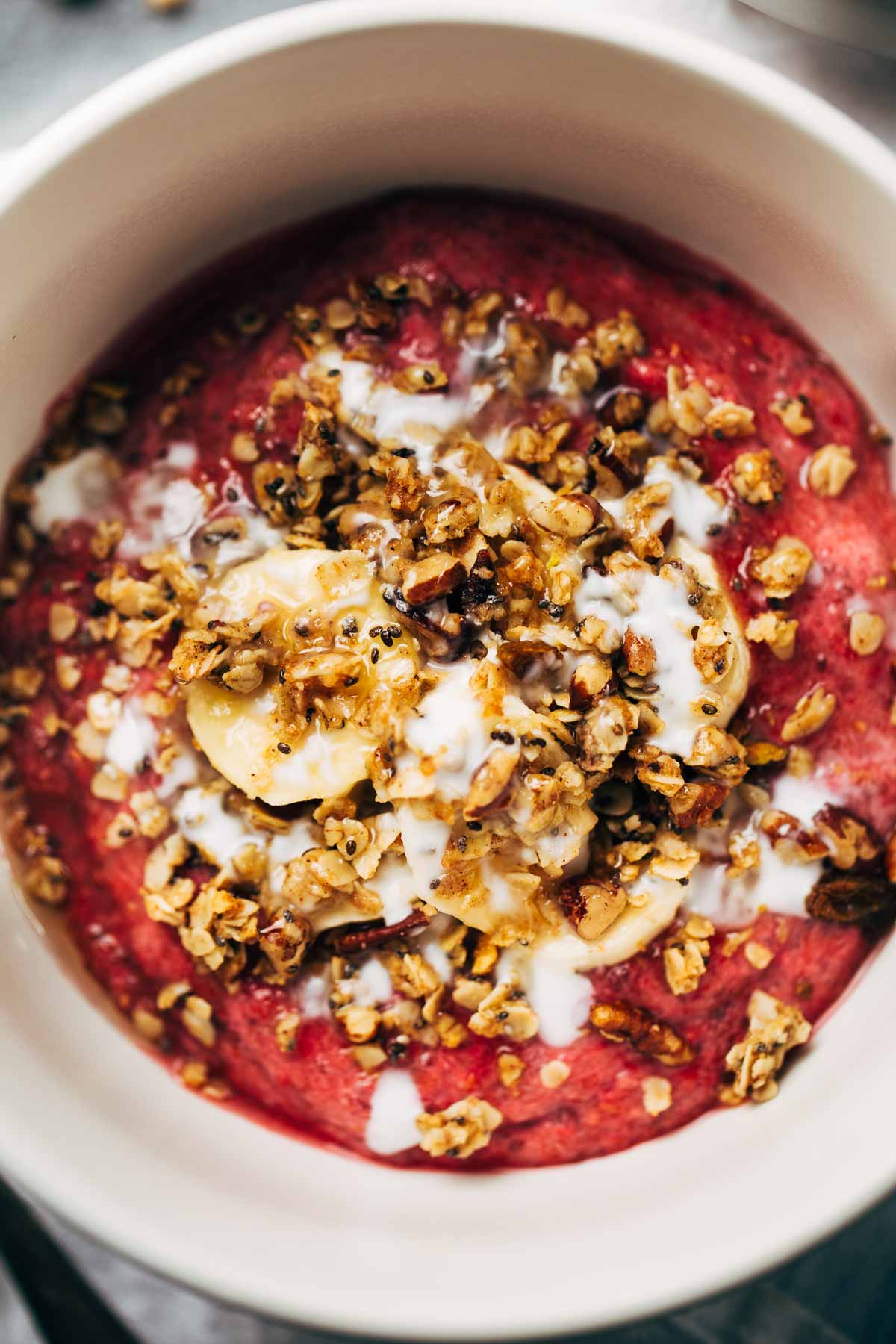 The red inner goddess raspberry breakfast smoothie bowl topped with granola, bananas, chia seeds, and honey.